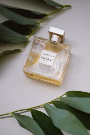 An image of a Gabrielle Essence Eau De Parfum bottle laying on a table next to some leaves.